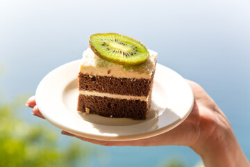Beautiful chocolate cake with a slice of kiwi on a white plate against the backdrop sea.