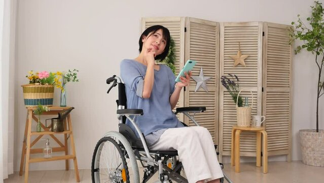 家でスマホを持って想像する車椅子に乗った障がい者女性