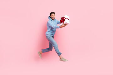 Full length photo of overjoyed nice man wear stylish blue clothes moving empty space carrying you gift isolated on pink color background