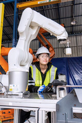 Young female asian service engineer holding robot controller operate robot arm automation factory