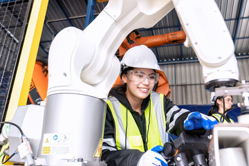 Young female asian service engineer holding robot controller operate robot arm automation factory