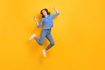 Fototapeta na wymiar Full size portrait of excited energetic girl jumping demonstrate v-sign empty space isolated on yellow color background
