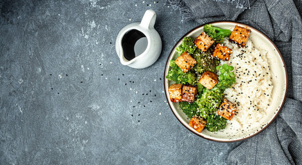 Asian vegan bowl with rice, broccoli and fried tofu on a dark background. Long banner format. top view