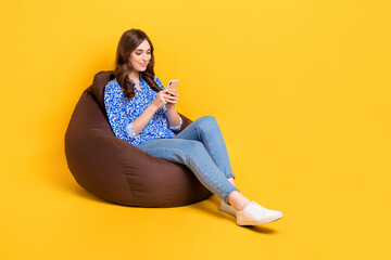 Full body portrait of pretty cheerful lady sit comfy bag use telephone typing post isolated on...