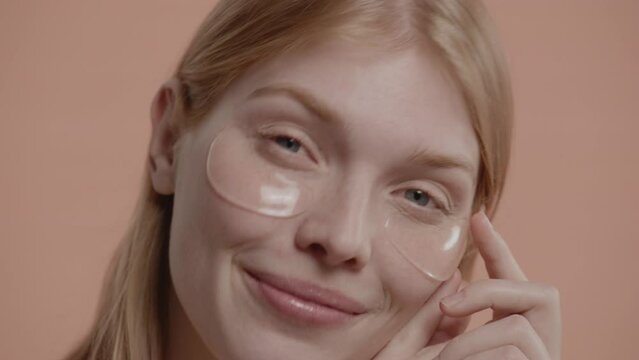Portrait of pure natural beautiful 20s Caucasian female using eye patches against pastel colored background