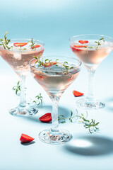 Glasses with cold pink champagne or punch with wine strawberries, ice and rosemary on blue background