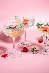 drink cocktail with ice in a glass on pink background. refreshing fruit cocktail or punch with wine champagne, strawberries, ice and rosemary