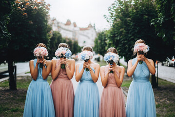 Bridesmaids at wedding with bouquets in hands. Girl in colored dresses for wedding. - obrazy, fototapety, plakaty