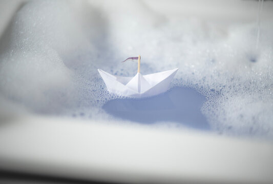 Kleines Papierschiff in der Badewanne mit Badeschaum