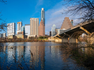 Vibrant Austin Texas city panoramic skyline behind trees, modern buildings, reflections on the Lady Bird Lake in Colorado River, and the Congress Avenue Bridge over the boardwalk