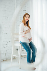 a red-haired pregnant girl in a light blouse and blue jeans