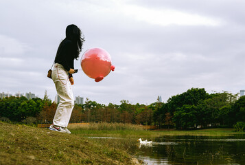 Obraz premium a woman stands by lake with a pink balloon