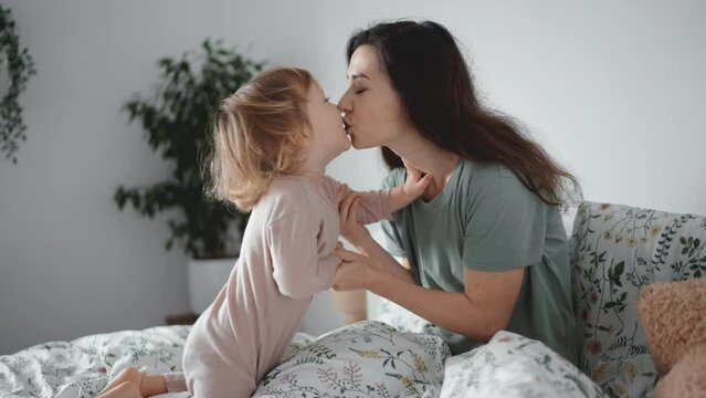 Authentic close up shot of young asian mother kiss and play with her curly toddler son in morning bedroom. Concept of children, baby, parenthood, childhood, life, maternity, motherhood relationship
