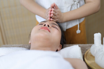 Fototapeta na wymiar Young woman enjoying massage in spa salon. Masseur doing massage the head of an Asian woman in the spa salon.