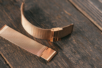 Close up of steel rose watch strap laying on the dark brown rustic wooden table.