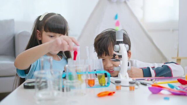 Education and Child and science concept.Cute elementary school boy and girl looking into microscope at home.Parent mother with daughter kid and son scientist making experiments in his home laboratory.