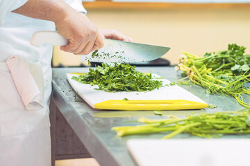Crop cook cutting parsley with knife in kitchen