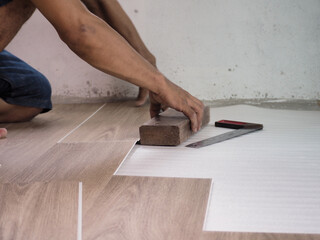 Fototapeta na wymiar A technician is cutting luxury vinyl floor tiles with a cutter to lay the floor before placing it on the leveling foam..