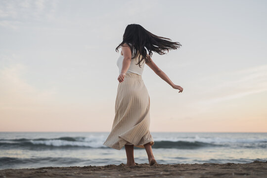 Anonymous young ethnic woman dancing on sandy seashore during summer vacation