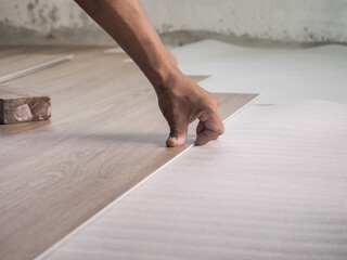 A technician is cutting luxury vinyl floor tiles with a cutter to lay the floor before placing it on the leveling foam..