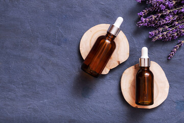 Dropper bottles with cosmetic oil on wooden podium with lavender flowers on concrete background