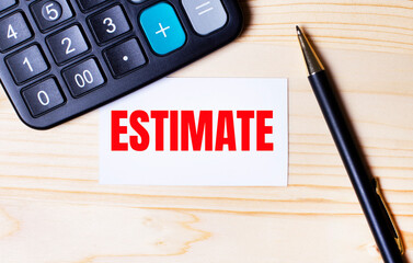 On a light wooden background, a black calculator, a pen and a business card with the text ESTIMATE