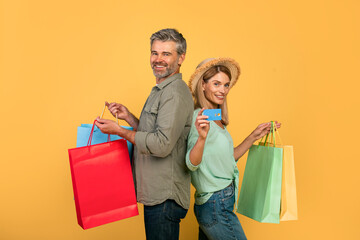 Portrait of middle aged caucasian spouses showing credit card and holding colorful shopper bags...