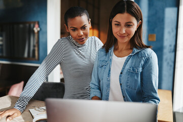 Smiling female entrepreneurs working online together at a cafe table