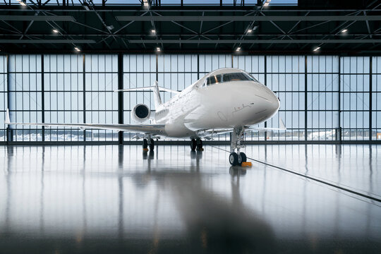 Private jet airplane at the huge white hangar waiting for maintenance and repair jobs. Expensive and luxury trip is waiting after a passengers. Business jet prepared for departure