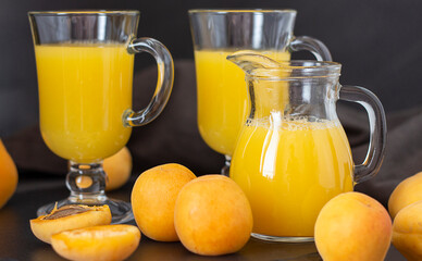 Apricot juice and apricots on a dark background. Apricots and apricot juice in a glass and decanter on a dark background.