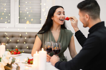 Beautiful young couple celebrating anniversary at home, eating strawberry
