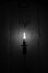 Einzelne Kerze leuchtet im Dunkel von einer Holzwand Weinfass mit der Nummer 3533, schwarz-weiß, Hintergrund