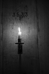 Single candle burning in the dark in front of a wooden wall of a wine barrel with the number 3533, black and white background