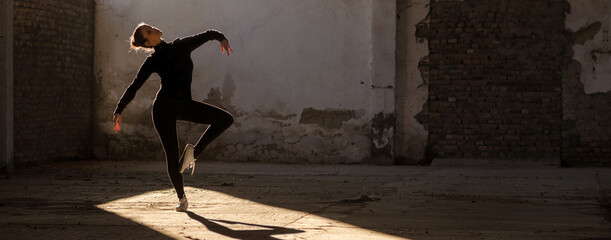 Fototapeta na wymiar Ballerina dancing in an abandoned building on a sunny day