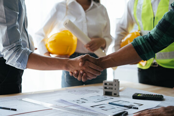 Construction workers, architects and engineers shake hands after completing an agreement in an...