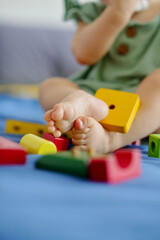 Feet of little girl playing with colorful wooden bricks