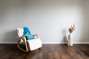 Minimalist interior with pillows and blanked thrown on modern rocking armchair. Dry plants...