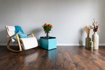 A living room interior featuring several vases filled with both fresh and dried flowers, a rocking armchair, and an ottoman converted into a serving table. The setting serves as a background for video