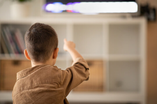 European small kid watch video, pointing finger at tv set, sits on floor in living room interior, back, close up