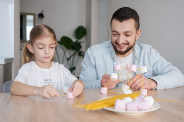Cute child girl with father playing and creating with marshmallows and spaghetti. Child concentrated with  building a molecule model. focus on girl.
