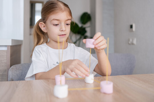 child girl playing and creating molecular shapes model from marshmallow and spaghetti. School kid using molecular handmade model for studying physics.