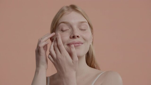 Portrait of pure natural beautiful 20s Caucasian female using eye patches against pastel colored background