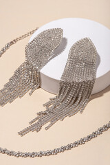 A set of jewelry from a pair of earrings and a necklace on a white podium.