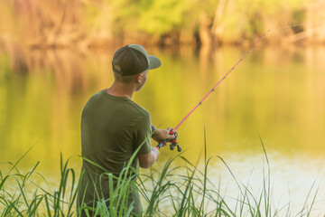 soft light photograph of a  teenage boy fishing from the side of the lake with the trees reflecting...