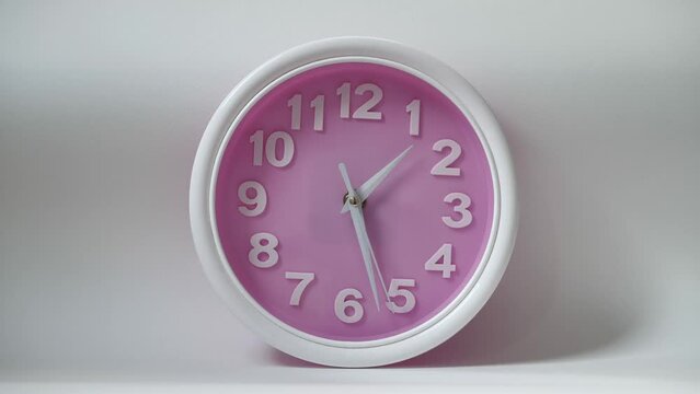 Portrait of clock isolated on a white background with a pink dial and white numerals. The concept of time clock is depicted. The hands of the clock move smoothly showing the transience of time.