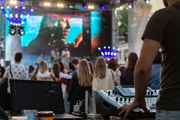 professional DJ music mixer, laptop at party festival with crowd of people in background, low light