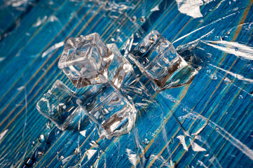 Ice cubes with water drops on a blue wooden surface.