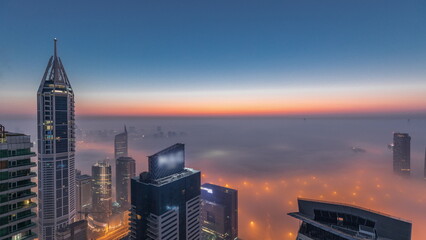 Rare early morning winter fog above the Dubai Marina skyline and skyscrapers lighted by street lights aerial night to day .