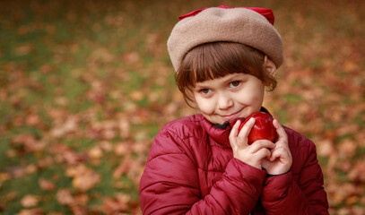 A beautiful girl is holding a ripe apple. Juicy healthy fruit in the hands of a child. Baby in the park outdoors.
