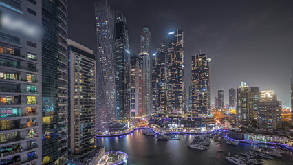 Panorama showing Dubai marina tallest skyscrapers and yachts in harbor aerial night .